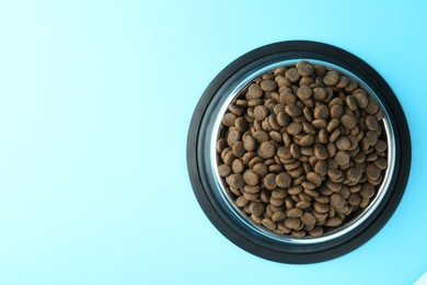 Photo of Dry pet food in feeding bowl on light blue background, top view. Space for text