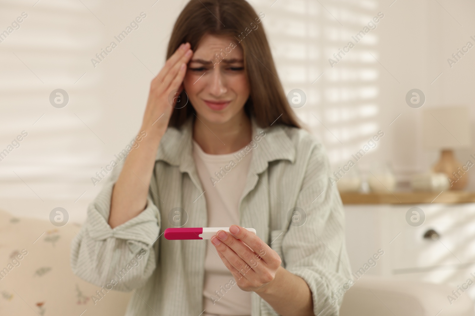 Photo of Upset woman with negative pregnancy test at home, selective focus