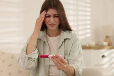 Photo of Upset woman with negative pregnancy test at home, selective focus