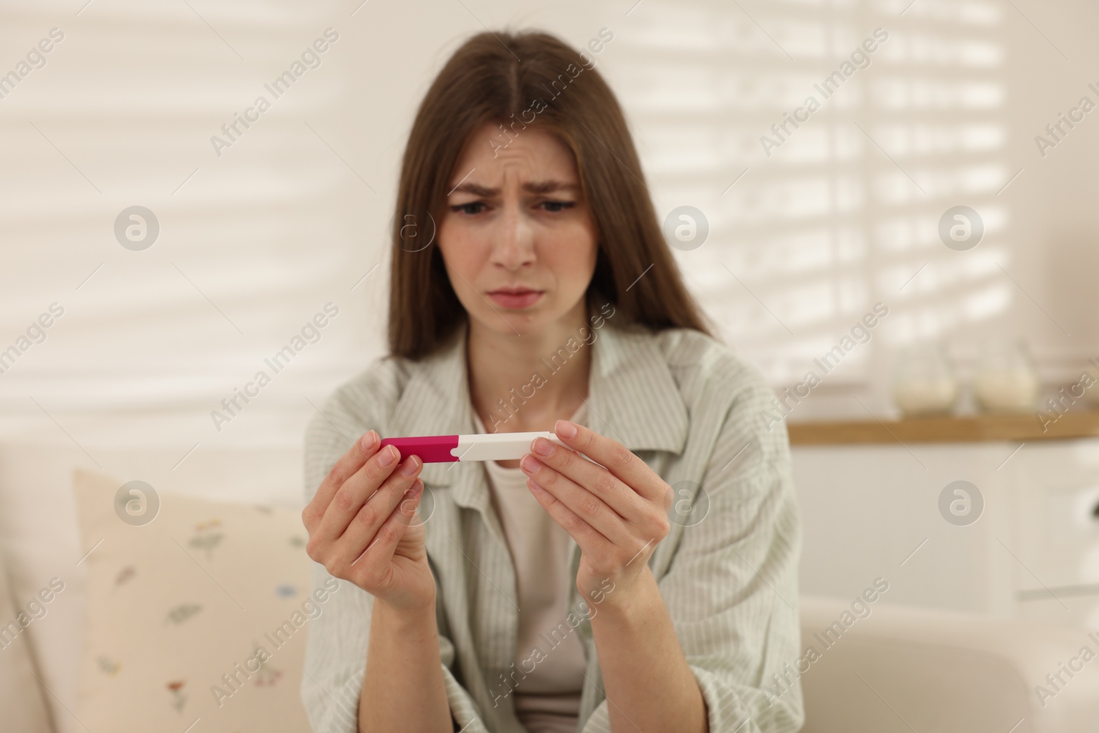 Photo of Upset woman with negative pregnancy test at home, selective focus