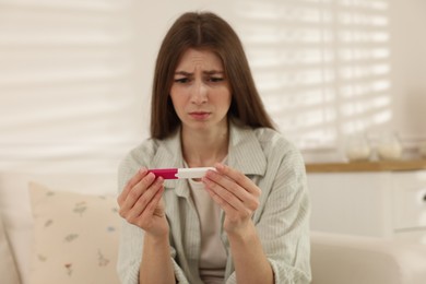 Photo of Upset woman with negative pregnancy test at home, selective focus