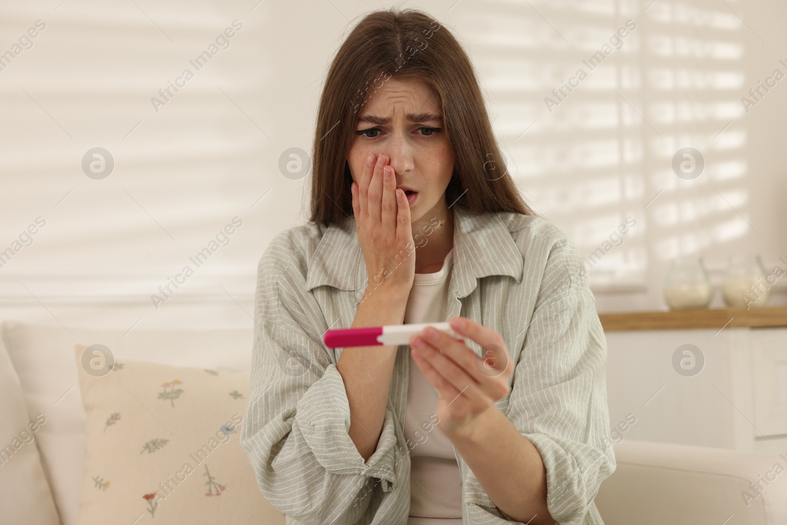 Photo of Upset woman with negative pregnancy test on sofa at home