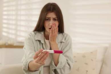 Photo of Upset woman with negative pregnancy test on sofa at home, selective focus