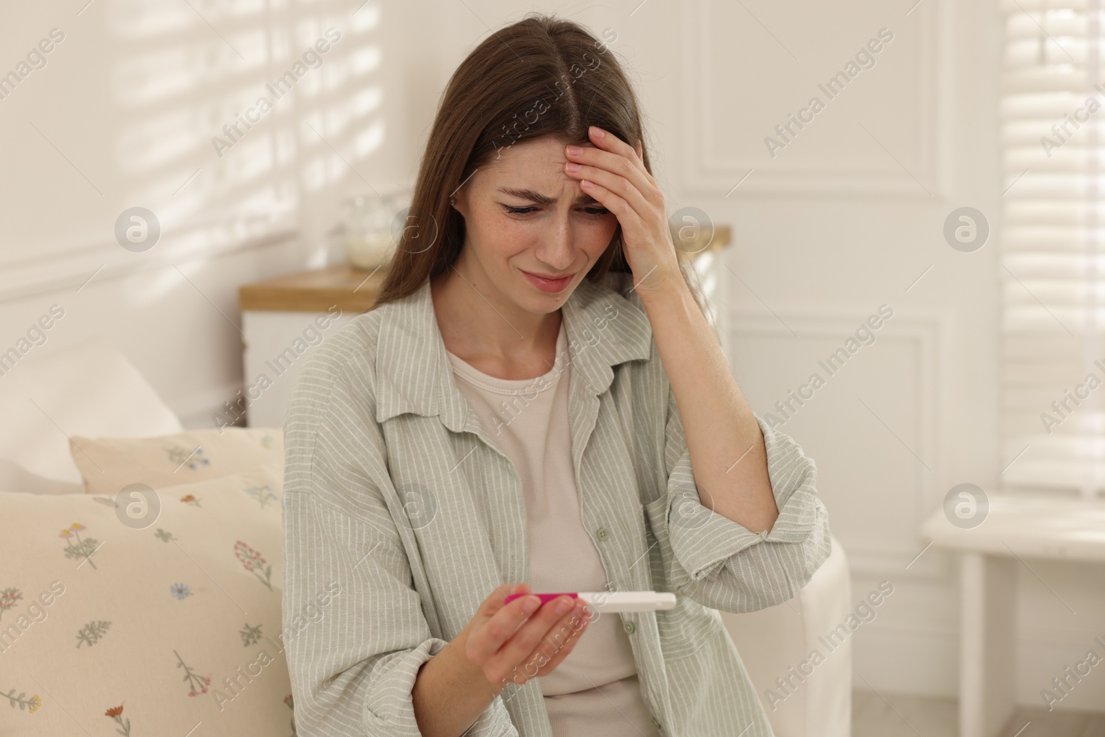 Photo of Upset woman with negative pregnancy test on sofa at home