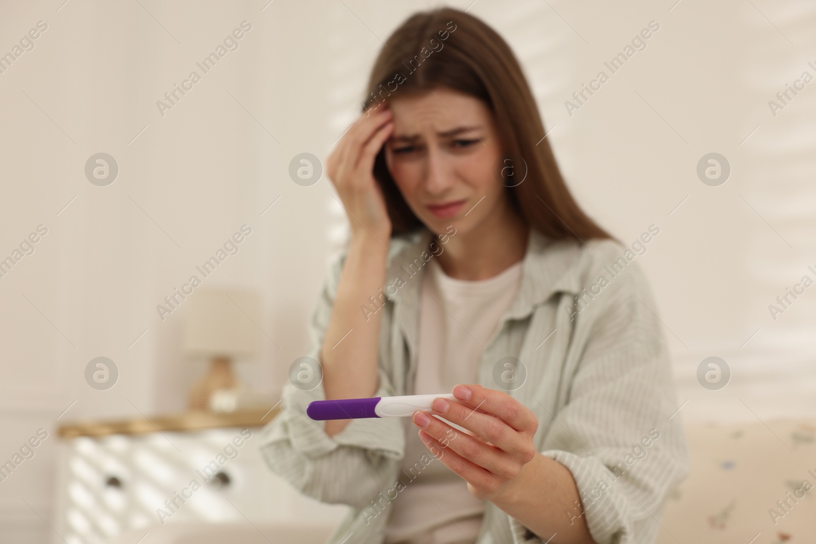 Photo of Upset woman with negative pregnancy test at home, selective focus. Space for text