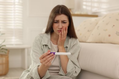 Photo of Upset woman with negative pregnancy test at home, selective focus