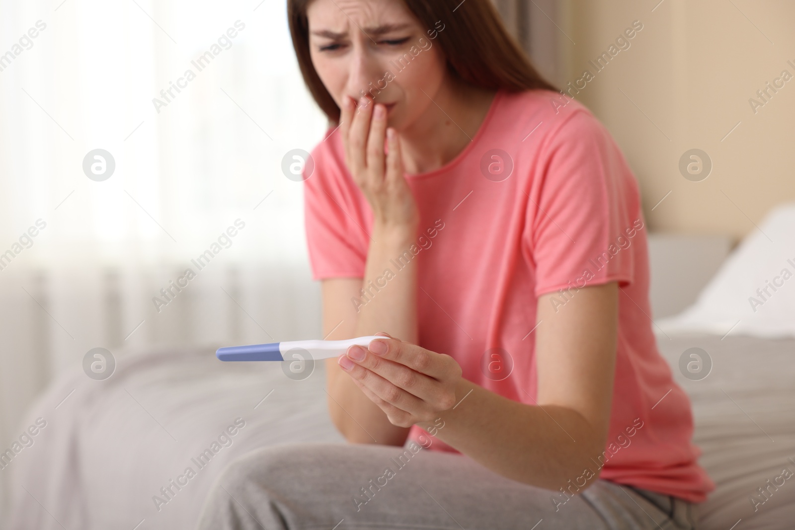 Photo of Upset woman with negative pregnancy test on bed at home, selective focus