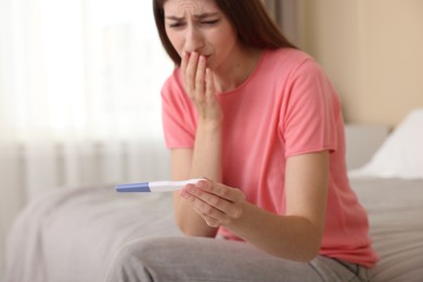 Photo of Upset woman with negative pregnancy test on bed at home, selective focus