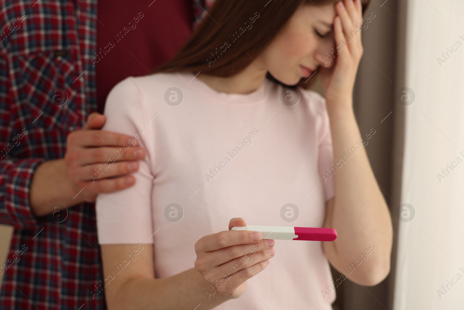 Photo of Upset woman with negative pregnancy test indoors, selective focus. Man supporting his wife at home