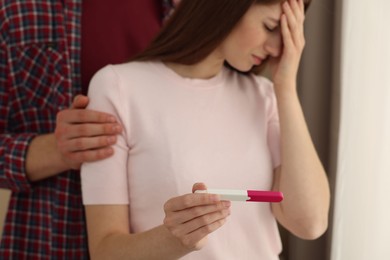 Photo of Upset woman with negative pregnancy test indoors, selective focus. Man supporting his wife at home