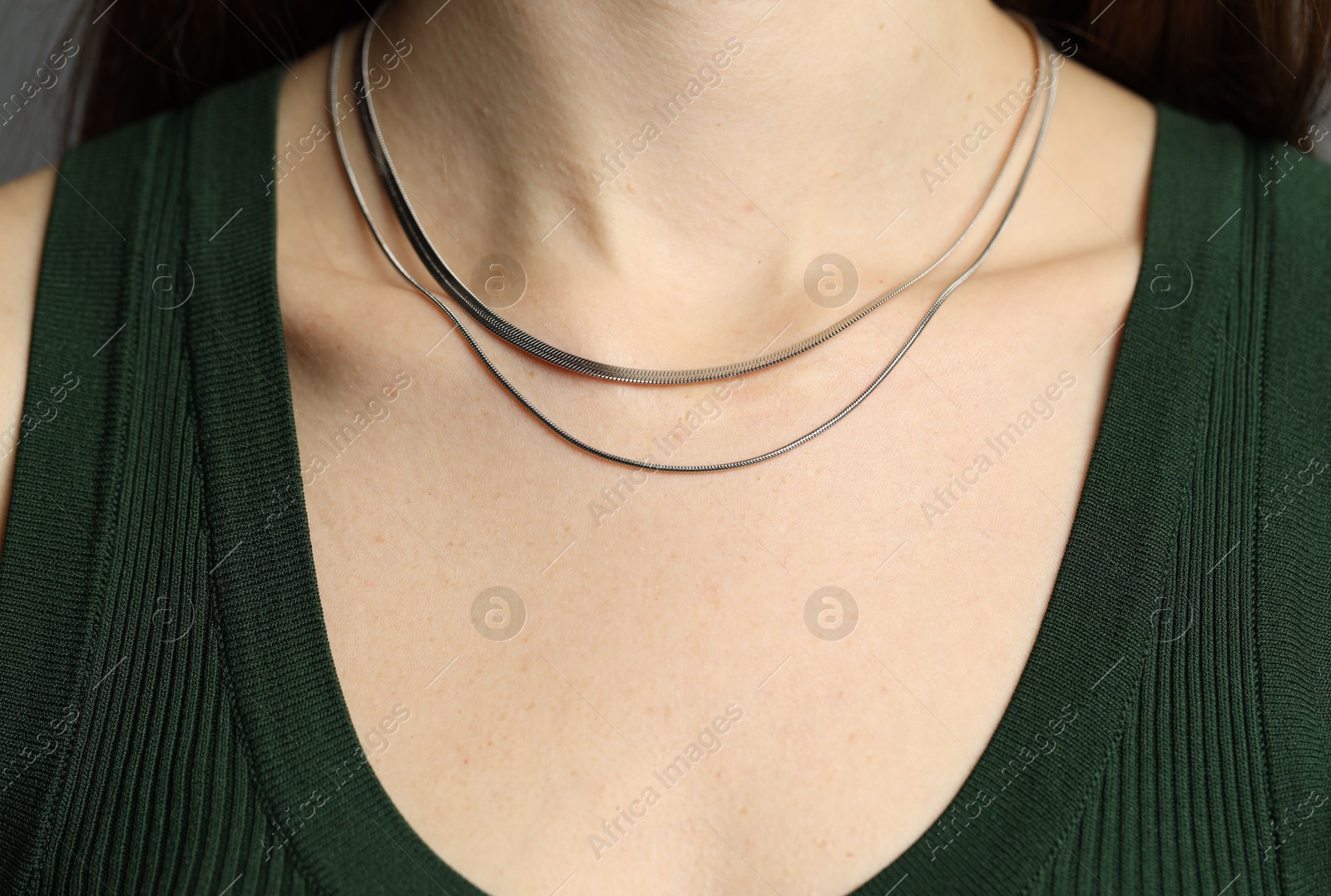 Photo of Woman wearing layered silver necklace on grey background, closeup