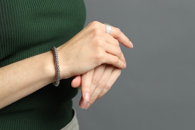 Photo of Woman wearing stylish silver bracelet and ring on grey background, closeup. Space for text