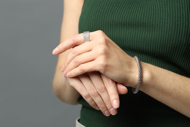 Photo of Woman wearing stylish silver bracelet and ring on grey background, closeup