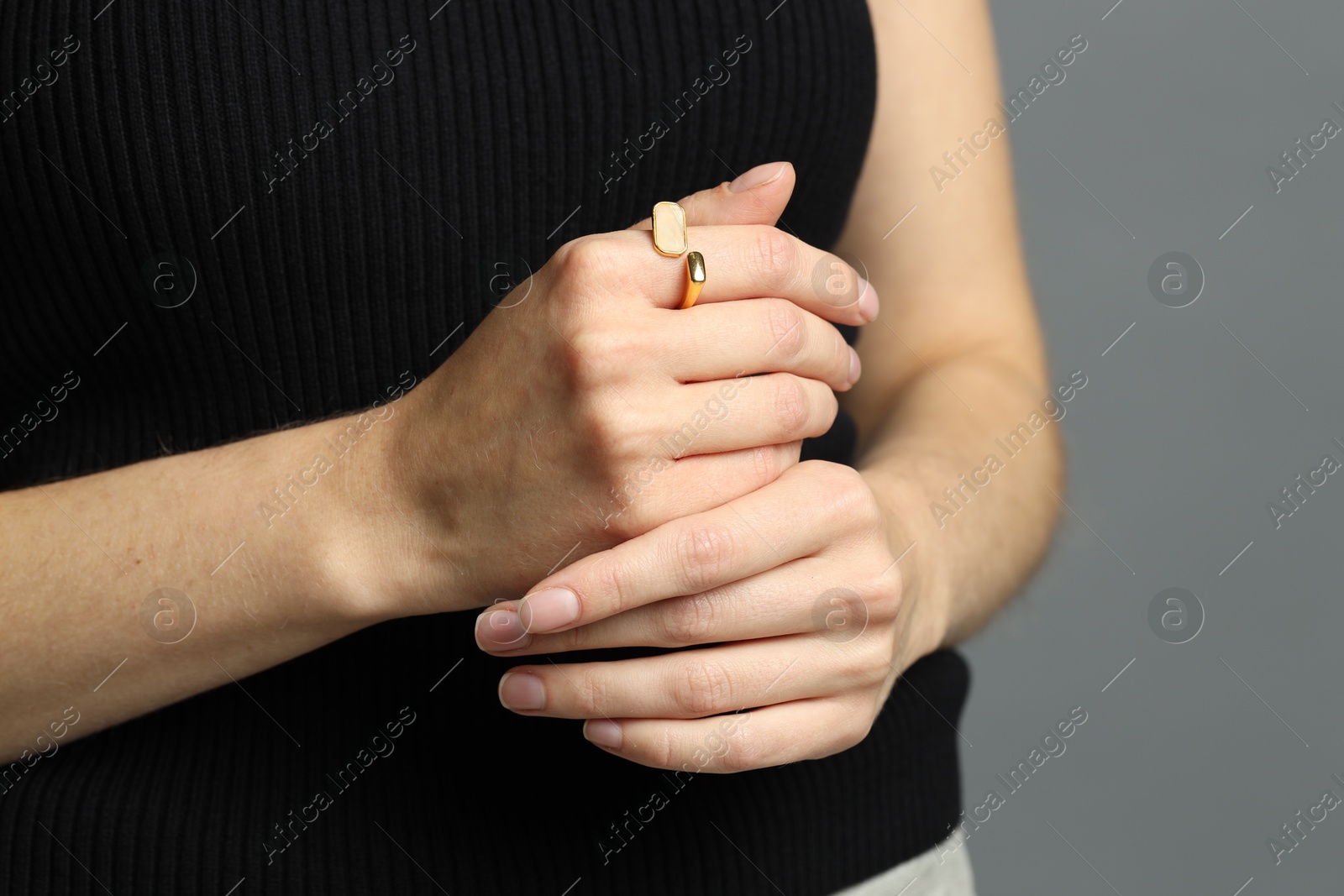 Photo of Woman wearing beautiful golden ring on grey background, closeup