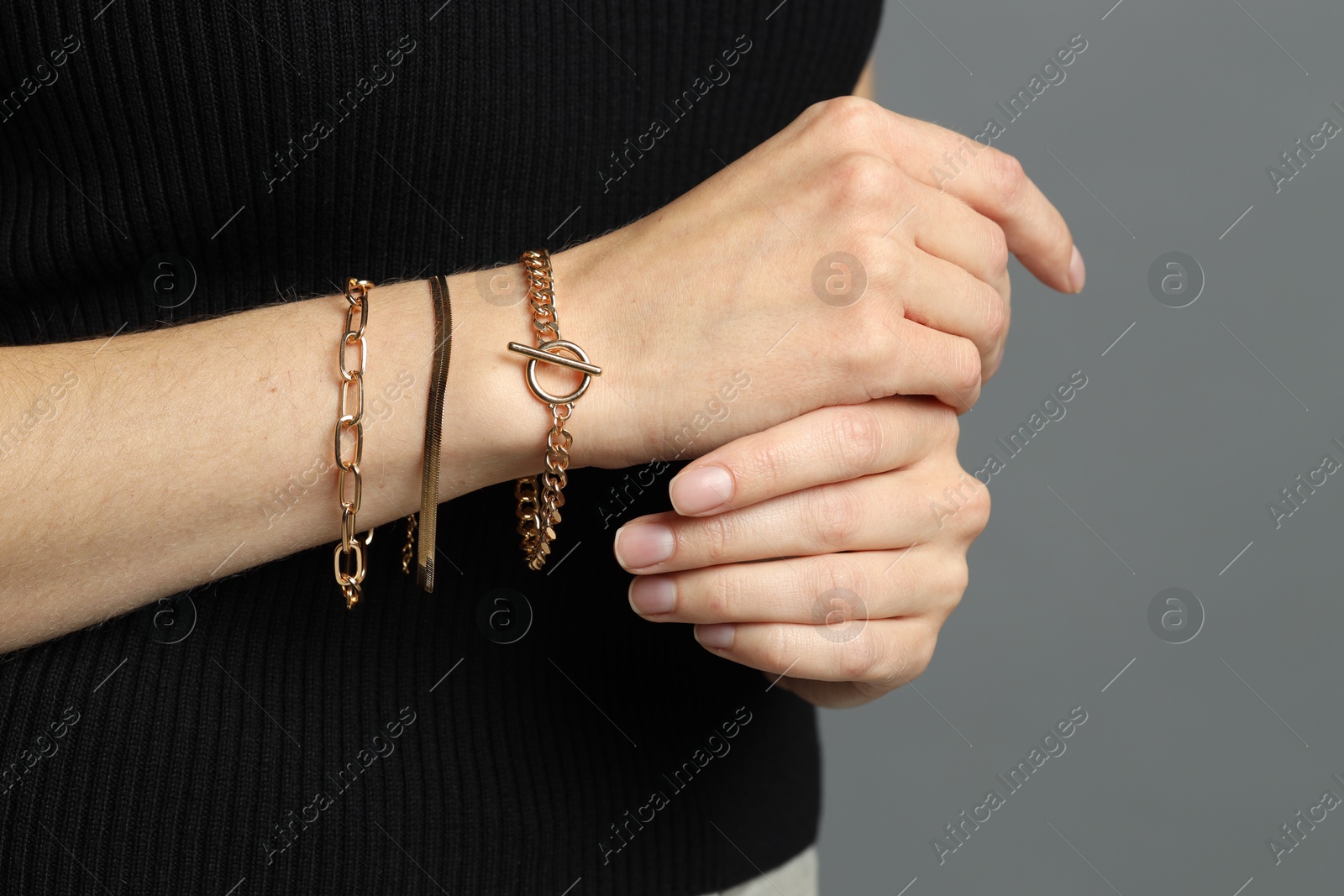 Photo of Woman wearing trendy golden bracelets on grey background, closeup