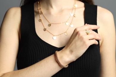 Photo of Woman wearing beautiful golden jewellery on grey background, closeup