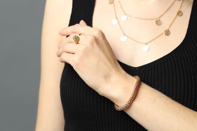 Woman wearing beautiful golden jewellery on grey background, closeup