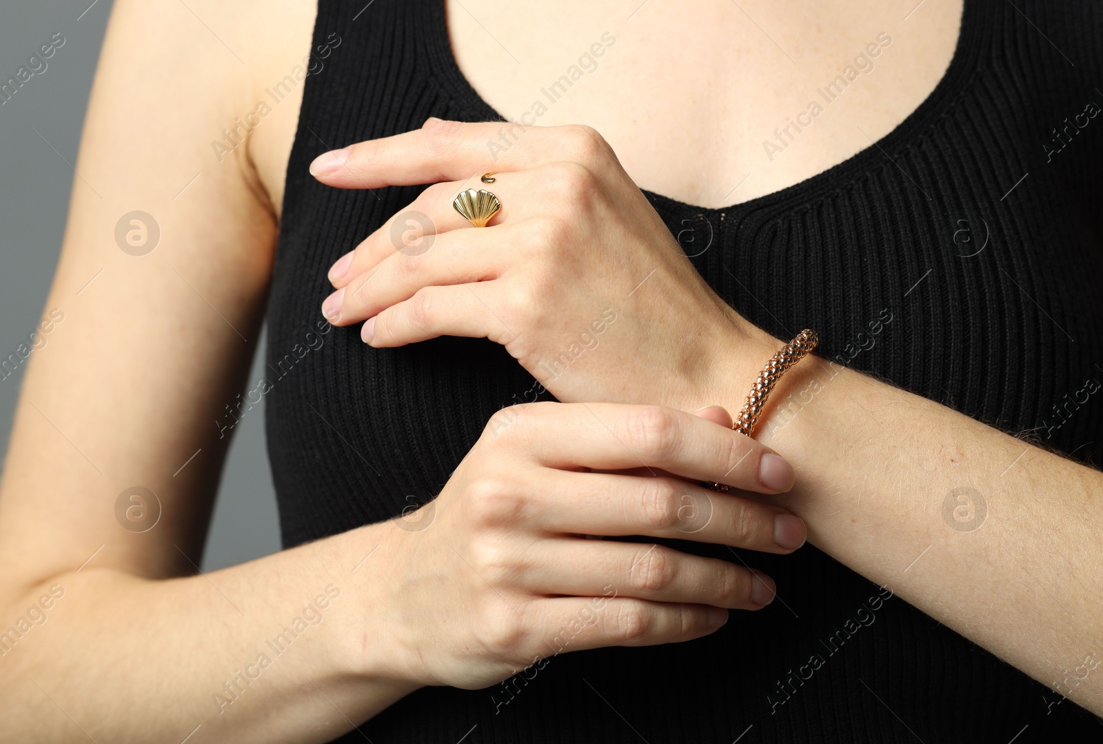 Photo of Woman wearing elegant golden bracelet and ring on grey background, closeup