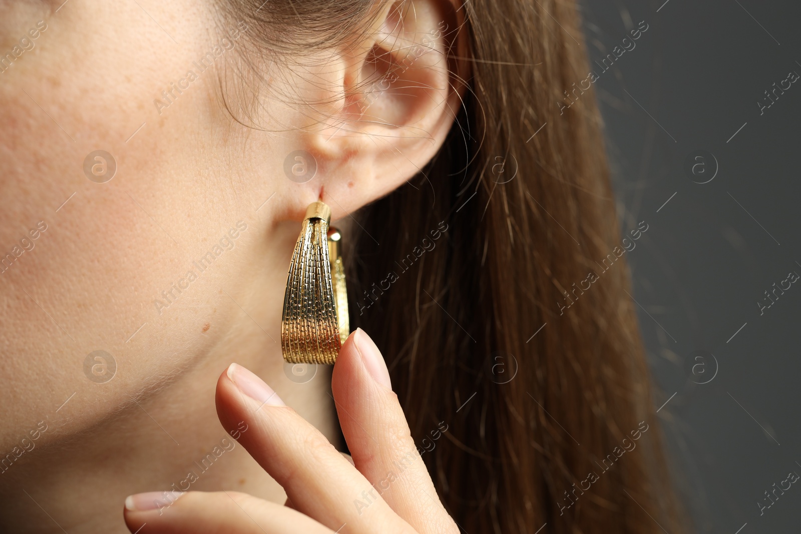 Photo of Woman wearing beautiful golden earring on grey background, closeup