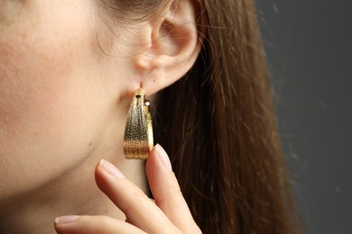 Photo of Woman wearing beautiful golden earring on grey background, closeup