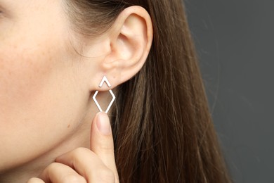 Woman wearing beautiful silver earring on grey background, closeup