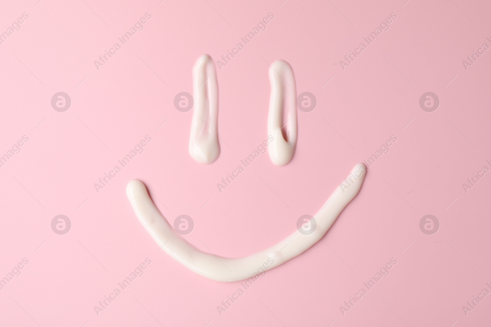 Photo of Smiling face made of cream on pink background, top view. Samples of cosmetic product