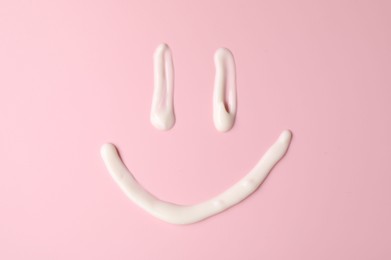 Photo of Smiling face made of cream on pink background, top view. Samples of cosmetic product