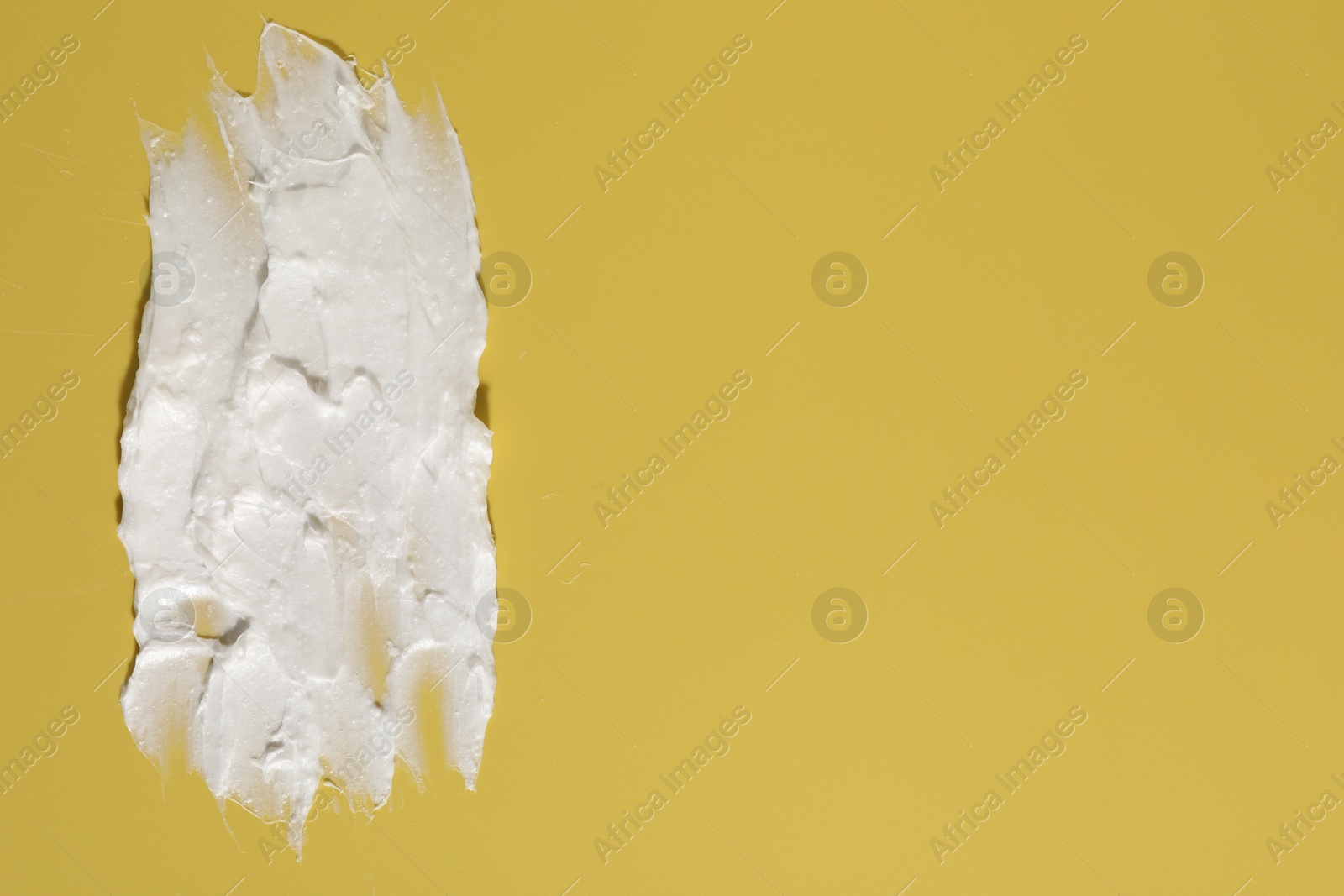 Photo of Cream on dark yellow background, top view and space for text. Sample of cosmetic product