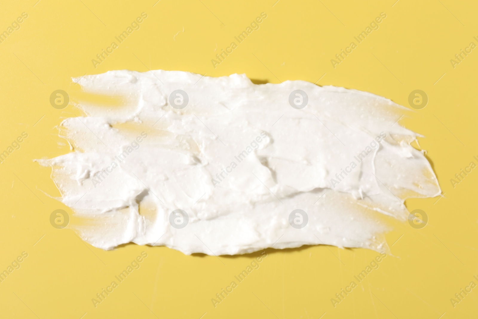 Photo of Cream on yellow background, closeup. Sample of cosmetic product