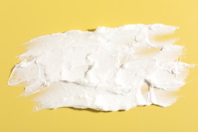 Photo of Cream on yellow background, closeup. Sample of cosmetic product