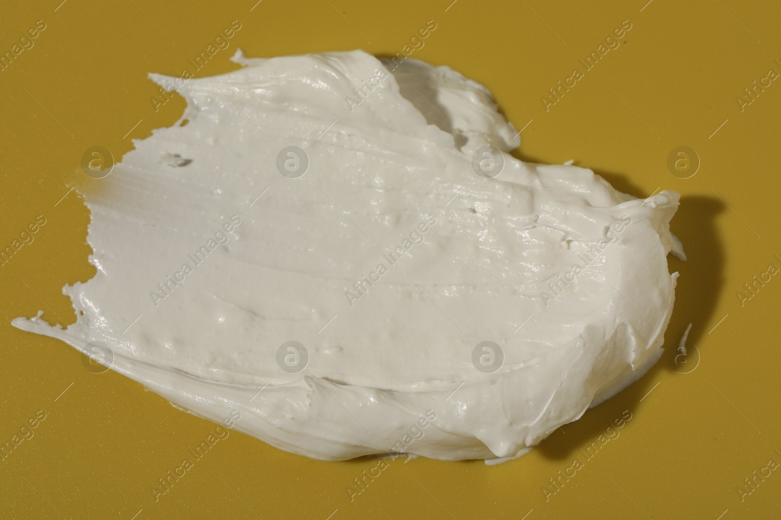 Photo of Cream on dark yellow background, closeup. Sample of cosmetic product