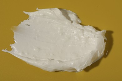 Cream on dark yellow background, closeup. Sample of cosmetic product