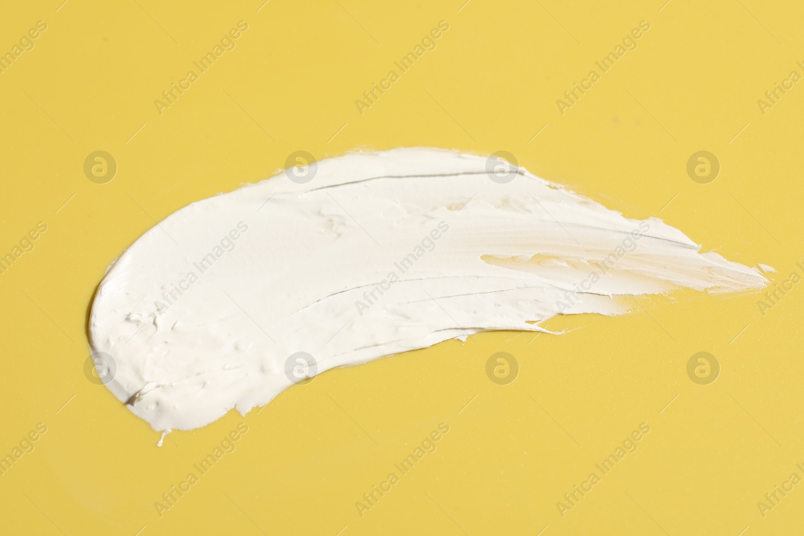 Photo of Cream on yellow background, top view. Sample of cosmetic product