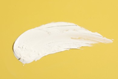 Photo of Cream on yellow background, top view. Sample of cosmetic product