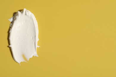 Photo of Cream on yellow background, top view and space for text. Sample of cosmetic product