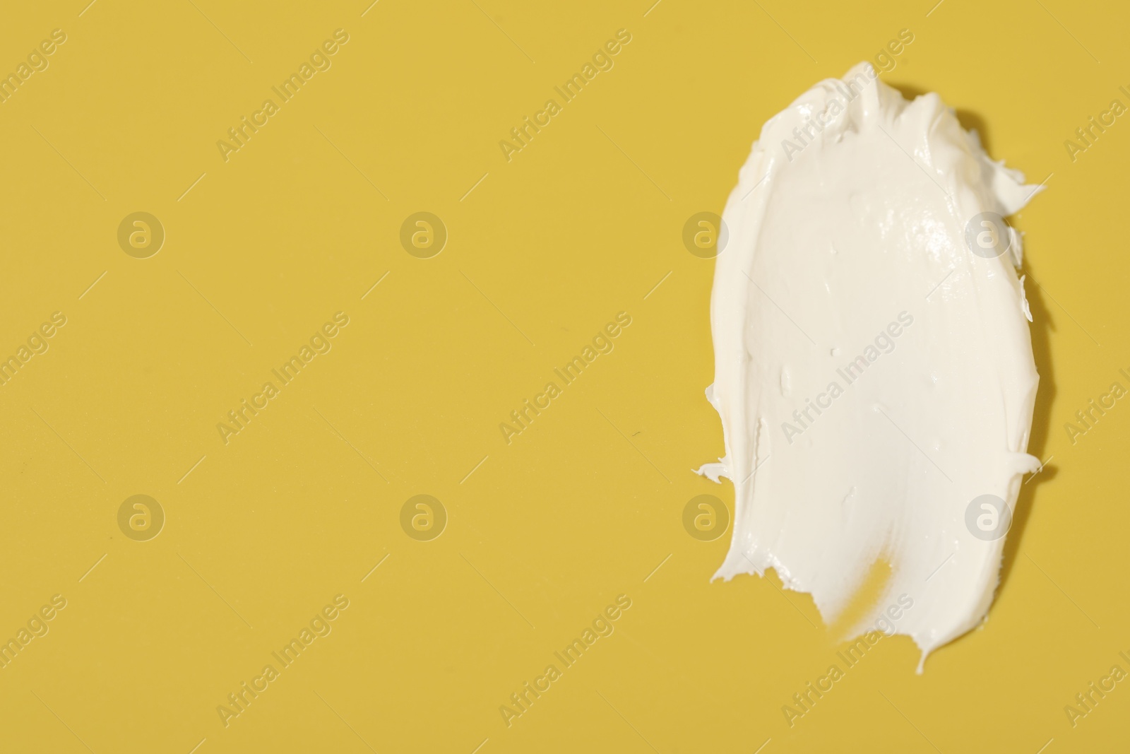 Photo of Cream on yellow background, top view and space for text. Sample of cosmetic product