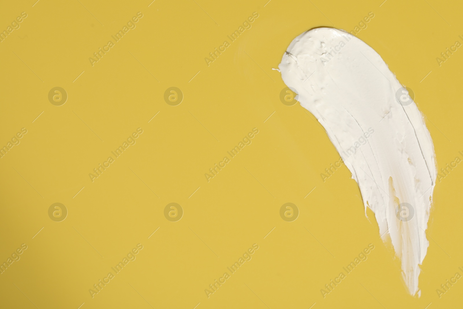 Photo of Cream on yellow background, top view and space for text. Sample of cosmetic product