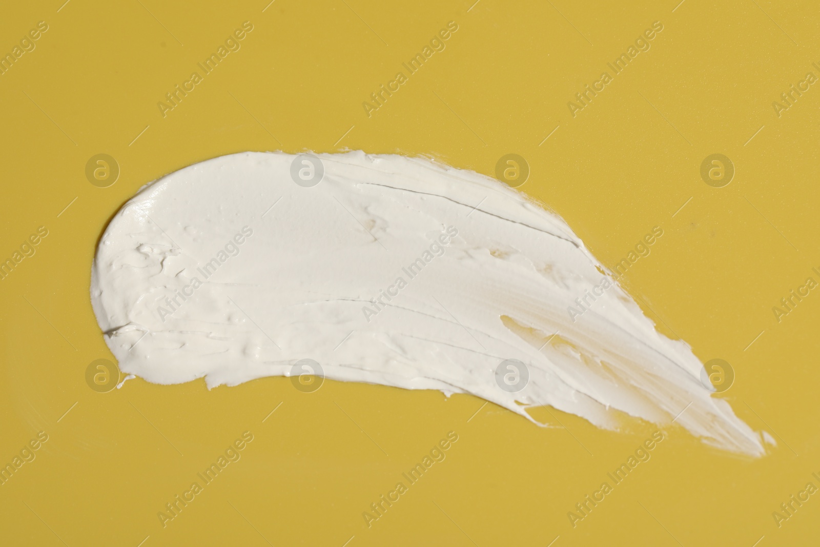 Photo of Cream on yellow background, top view. Sample of cosmetic product