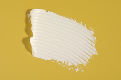 Photo of Cream on yellow background, top view. Sample of cosmetic product