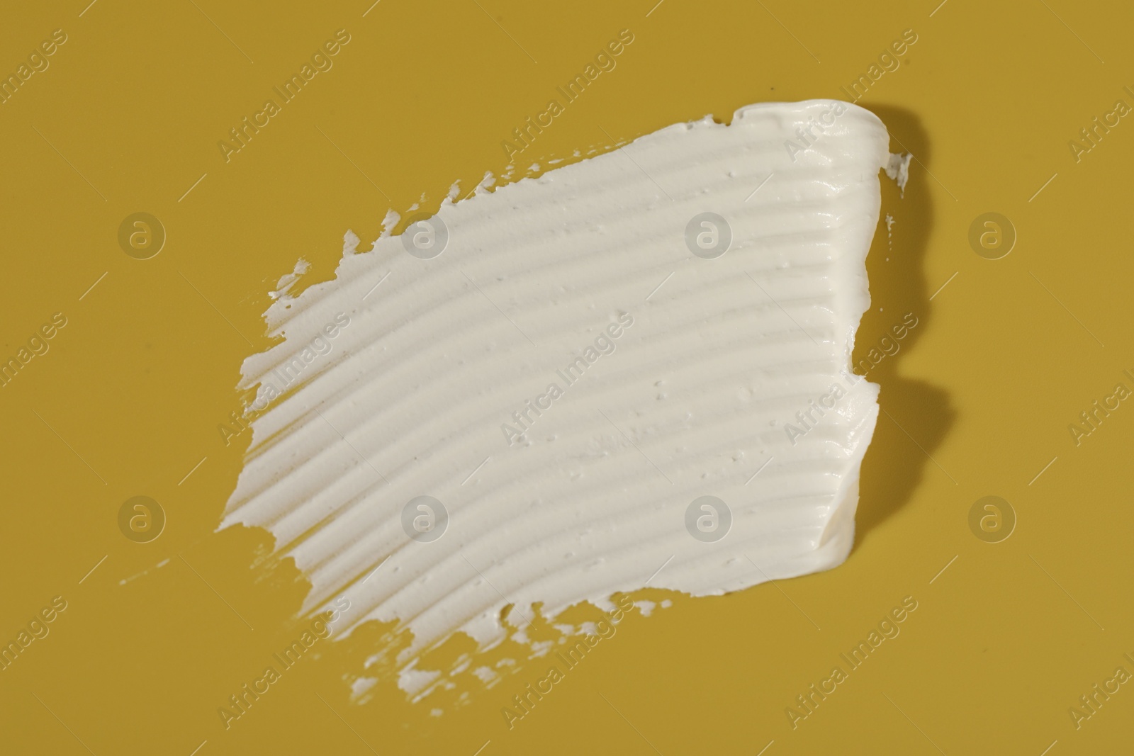 Photo of Cream on dark yellow background, top view. Sample of cosmetic product