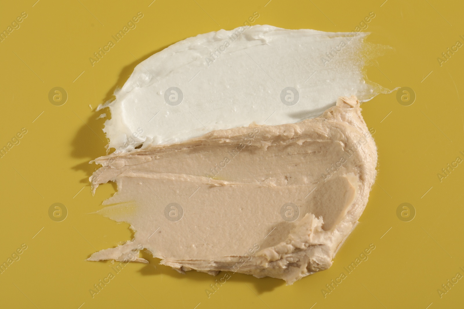 Photo of Samples of cream on yellow background, top view