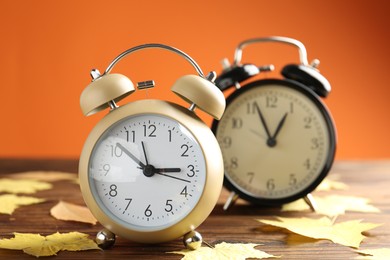 Autumn time. Alarm clocks and golden leaves on wooden table