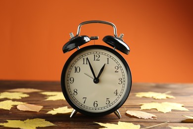 Photo of Autumn time. Alarm clock and golden leaves on wooden table