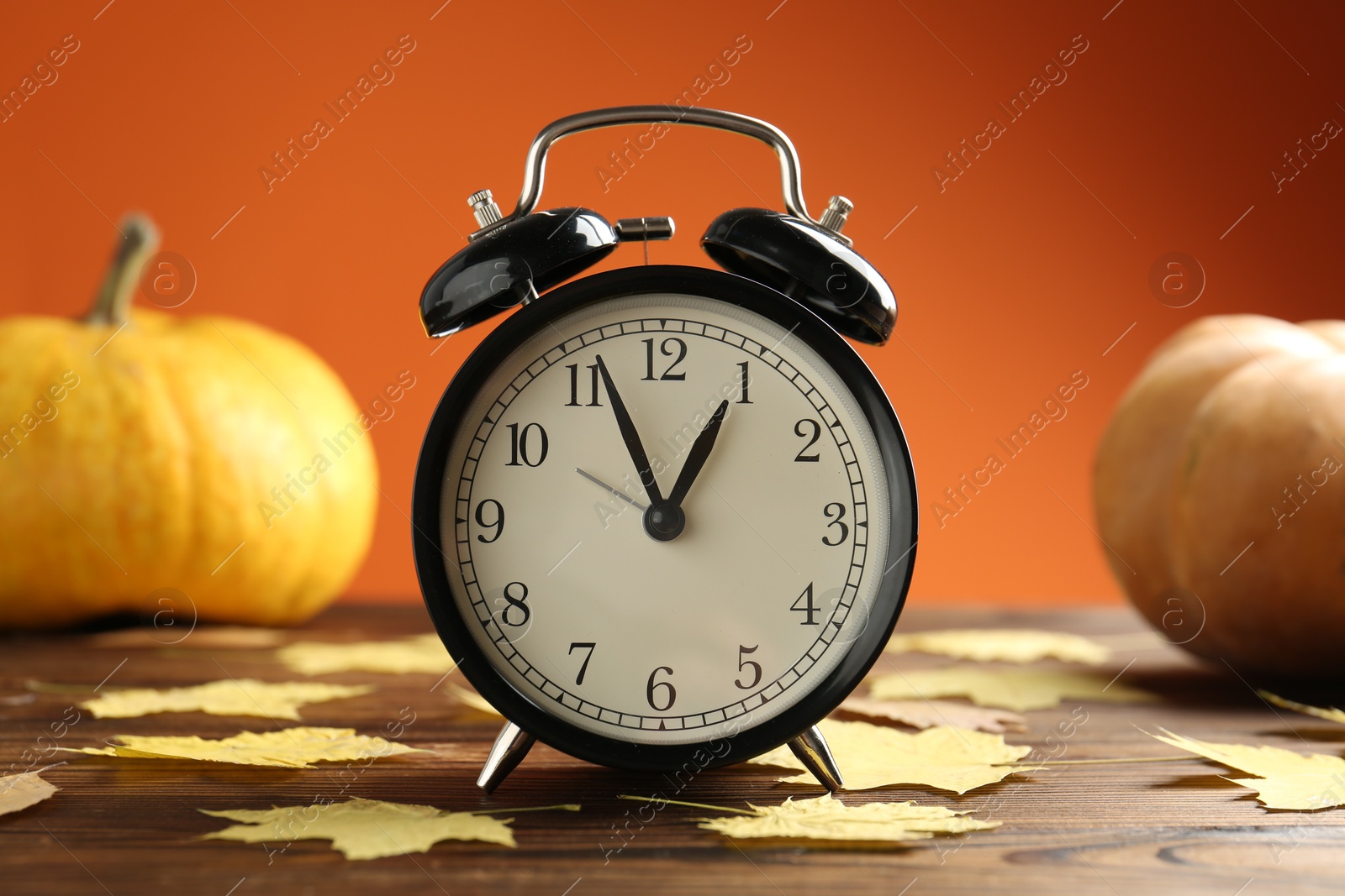 Photo of Autumn time. Alarm clock and golden leaves on wooden table