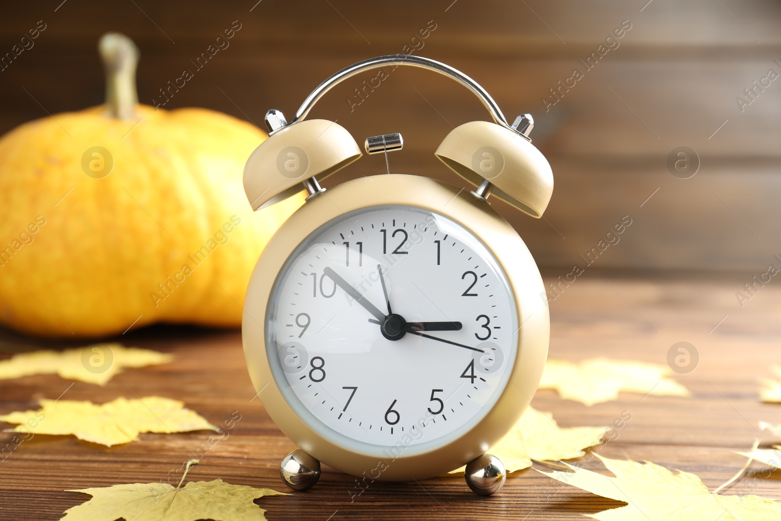 Photo of Autumn time. Alarm clock and golden leaves on wooden table