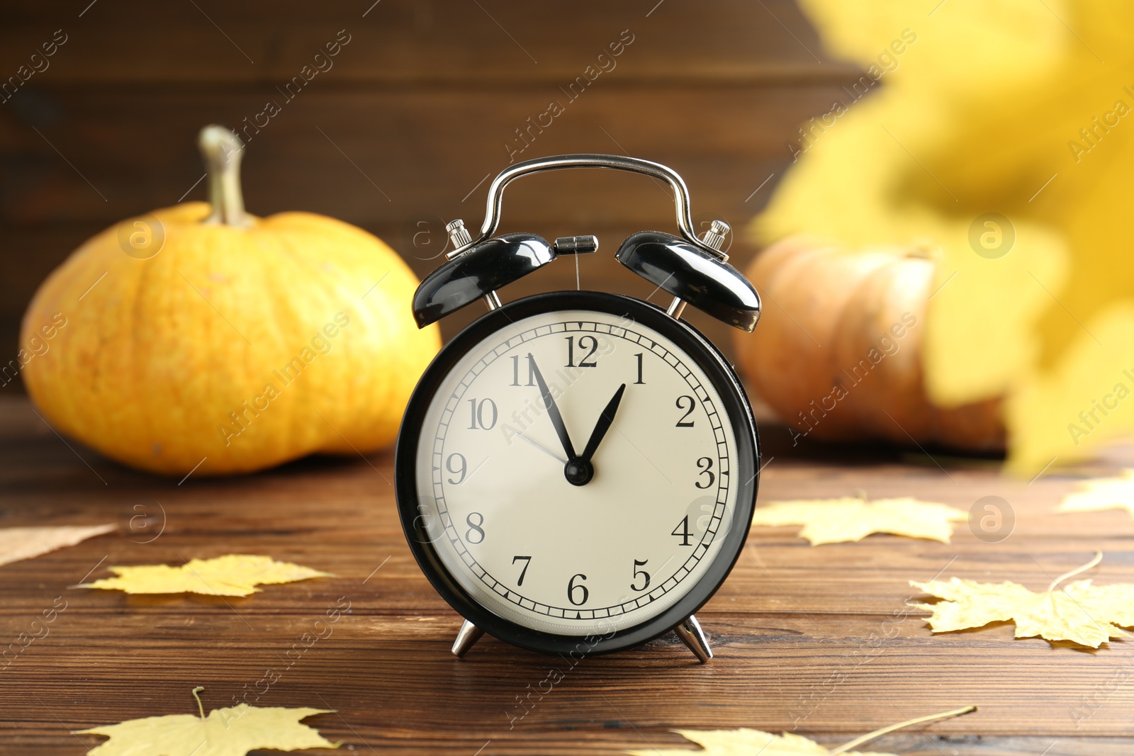 Photo of Autumn time. Alarm clock and golden leaves on wooden table