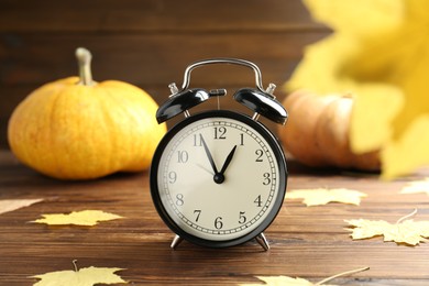 Photo of Autumn time. Alarm clock and golden leaves on wooden table