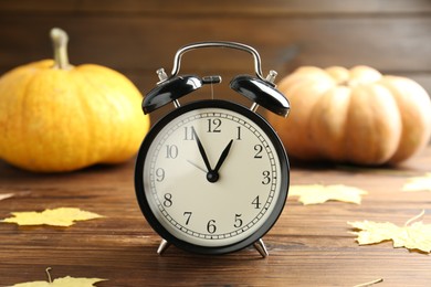 Autumn time. Alarm clock and golden leaves on wooden table