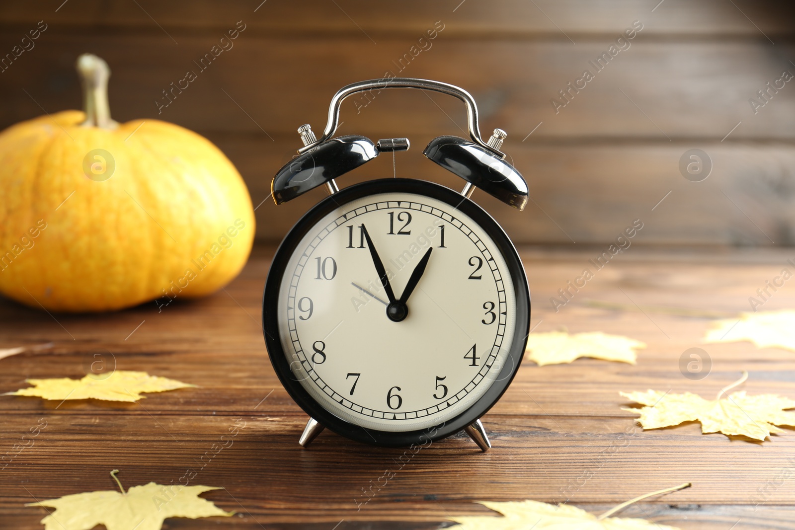 Photo of Autumn time. Alarm clock and golden leaves on wooden table