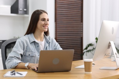 Photo of Programmer working on laptop and computer at wooden desk indoors